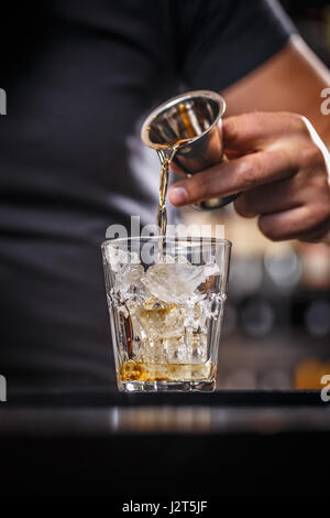 Barman is pouring alcohol from a jigger into a glass over ice; preparing an alcoholic cocktails Stock Photo