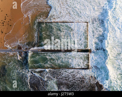 VERTICAL AERIAL VIEW. Swimmers in the safety of a rockpool from a rough sea. Austinmer, New South Wales, Australia. Stock Photo