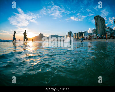 RIO DE JANEIRO - FEBRUARY 2, 2013: Silhouettes pass in front of the sunset on the shore of Ipanema Beach. Stock Photo