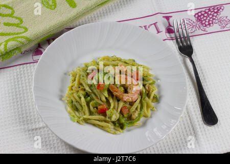 Trofie pasta with prawn (shrimp), broccoli and zucchini (courgette) in white dish on white kitchen cloth with fork - Italian delicious seafood recipe Stock Photo