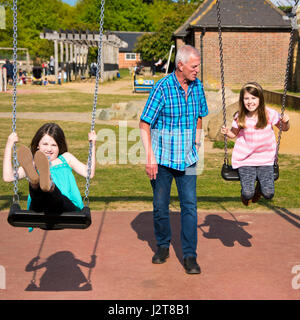 Square portrait of girls being pushed on the swings by their granddad in a park. Stock Photo