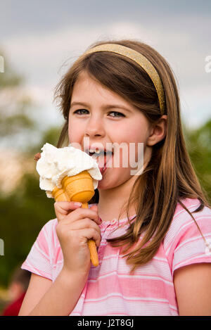 Vertical portrait of a young girl eating an ice cream in the sun. Stock Photo