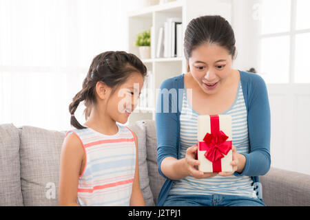 touched mother happy to open the gift of lovely daughter was pleasantly surprised sitting together at home on the sofa in mother's day festival holida Stock Photo