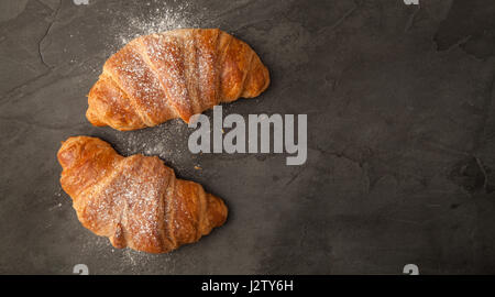 Top View of two fresh croissants dusted with icing sugar on grey slate Stock Photo