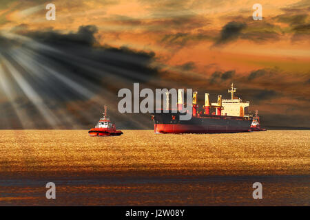 Tugboats towing a large cargo ship on sea. Stock Photo