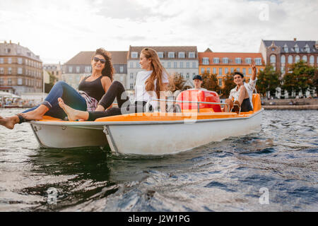Shot of group of young friends enjoying a ride on pedal boat. Teenagers relaxing on boat in the lake.