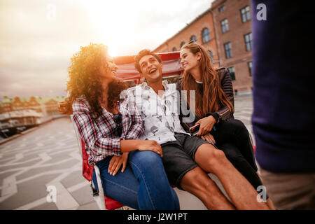 Cheerful teenage friends on tricycle. Young man and women riding on tricycle on road and having fun. Stock Photo