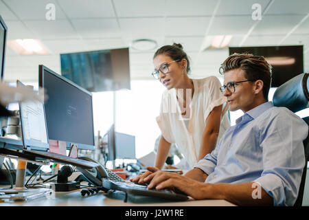 Mature businessman working on desktop computer with asian female colleague. Two office worker working together on computer. Stock Photo