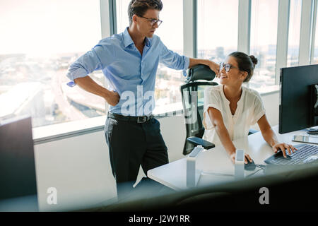 Smiling asian businesswoman working at their desk and looking at her colleague. Two business coworkers working together in modern office. Stock Photo