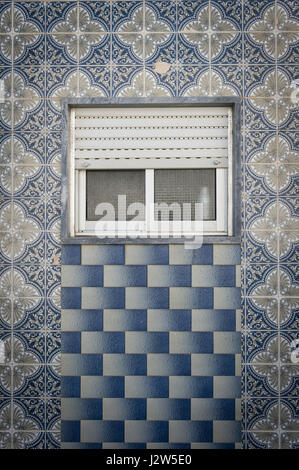Portuguese ceramic tiles in geometric patterns on the outside of a building with a shuttered window Stock Photo