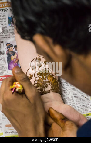 A Henna / Mehndi artist working on a bride's arm during a Henna party. Stock Photo