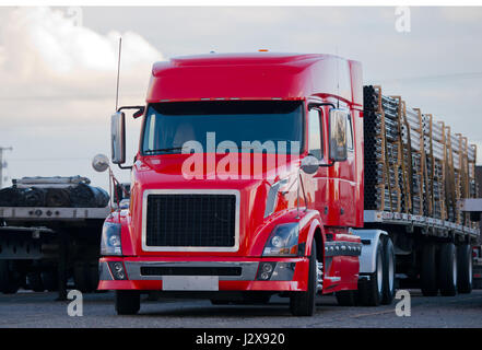 Powerful bright red semi truck with low cabin with modern accessories in stainless steel with a flat bed trailer, loaded with plastic pipes Stock Photo