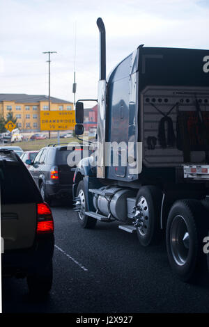 Large dark blue modern big rig semi truck with reflection on cabin driving on the road surrounded by cars standing in front of heavy traffic Stock Photo