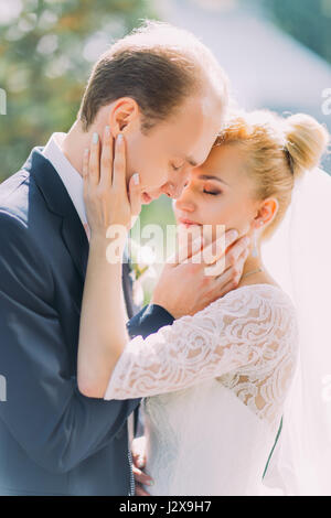 Stylish beautiful happy wedding couple kissing softly embracing in Botanical Garden Stock Photo