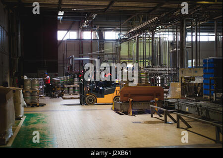 Warehouse employee in Overalls clothes, driver Reachtruck busy working on logistics Moving on loader pallets with beer kegs on line of factory for pro Stock Photo