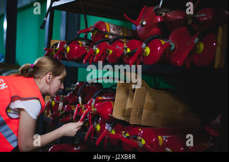 Checking fire extinguishers in the warehouse. Woman Engineer shall record and verify the presence of fire extinguishers Stock Photo