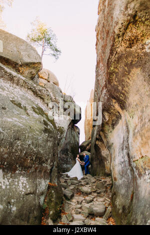 Young and beautiful bride with her elegant groom posing in weathered rock cleft Stock Photo