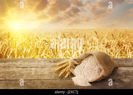 bran in bag and ears on table with ripe cereal field on the background. Food supplement to improve digestion. Dietary fiber. Product for healthy nutri Stock Photo