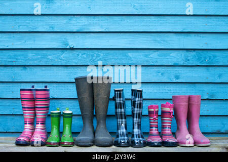 Many colorful rubber boots in front of a blue wooden wall Stock Photo