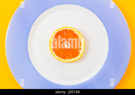 Top view of single grapefruit slice on plate centrally placed in frame creating concentric circles. Minimalist picture style with copy space for text Stock Photo