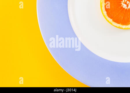 Top view of single grapefruit slice on plate diagonally placed on the side of the frame creating concentric semicircles. Minimalist picture-copy space Stock Photo
