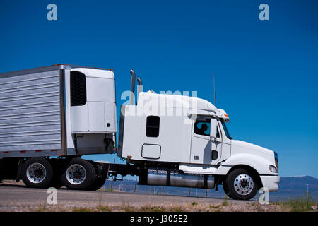 Big white truck with a trailer and a refrigeration unit on the road of the highway against the blue clear sky. Side view draws all the outlines Stock Photo