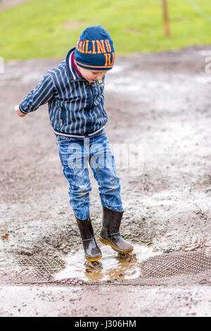 Day view excited boy jumps in a puddle. Stock Photo