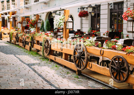 Exterior Of Cozy Outdoor Street Cafe In Retro Rural Rustic Style. On Wooden Wall Of Cafe Or Restaurant Hanging Wooden Wheels From Peasants Carts. Stock Photo