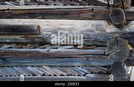 Old wooden unpainted wall of the house of round logs and chopped planks stacked between the logs Stock Photo