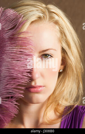 Beautiful blond woman hiding face with a pink feather Stock Photo