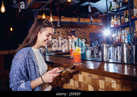 A girl with  cocktail smiles with tablet behind counter at the b Stock Photo