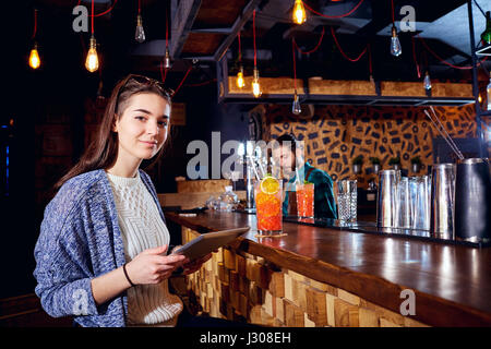 A girl with  cocktail smiles with tablet behind counter at the b Stock Photo