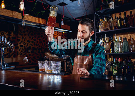 The barman with a beard pours alcohol into glasses in a bar Stock Photo