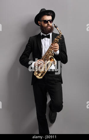 Saxophone player leaning against a gray wall Stock Photo