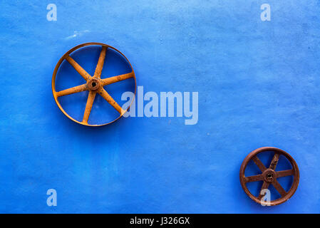 Blue colonial wall with rusty wheels on it near Merida, Mexico Stock Photo