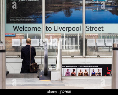 A passenger takes an escalator down to the station concourse at Liverpool Street combined Mainline Train and Underground station in central London Stock Photo