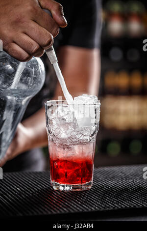 Bartender is pouring soda water, he is preparing a raspberry cocktail Stock Photo