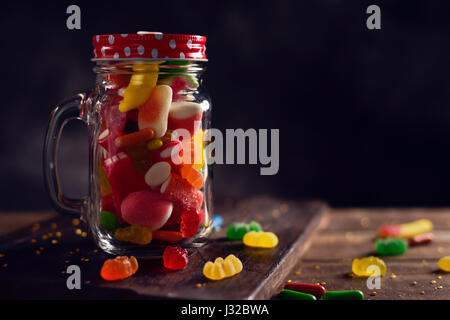 a mason jar full of candies with different flavors and colors, on a rustic wooden table Stock Photo