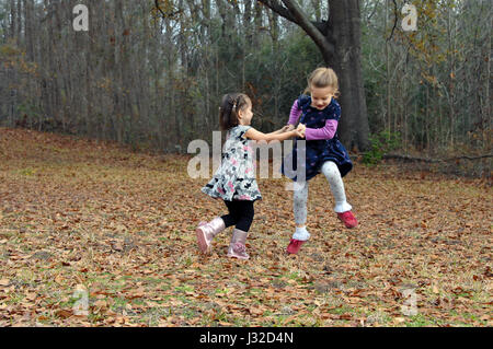 Two friends dance for joy in the Autumn leaves in Arkansas.  They are holding hands and jumping high and running in circles. Stock Photo