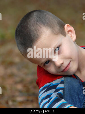 Hugging his knees are little boy, in red shirt and jeans, looks a very serious and thoughtful. Stock Photo
