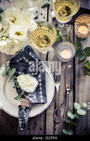 Table setting with white flowers, candles and glasses of champagne on an old vintage rustic wooden table. Vintage summer wedding table decoration, top Stock Photo