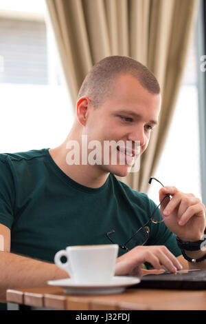 Handsome young man sitting, looking at the laptop and drinking coffee Stock Photo