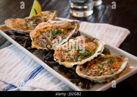 A flight of four oysters on the half shell, topped with bacon and pecorino, served on a bed of seaweed, in a restaurant setting Stock Photo