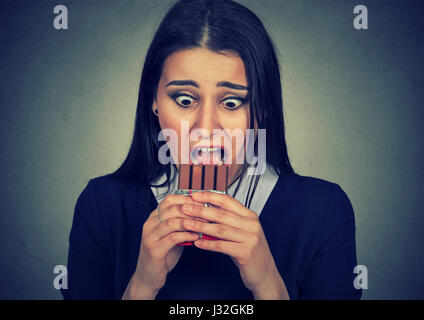 Portrait obsessed young woman tired of diet restrictions craving sweets chocolate isolated on gray background. Human face expression emotion. Nutritio Stock Photo