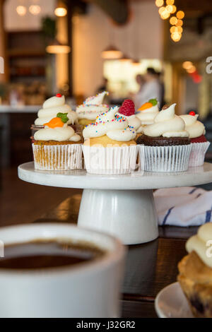 Gourmet assorted cupcakes displayed on a white ceramic cake stand inside a bakery Stock Photo