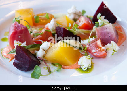 Close-up of roasted beet salad with heirloom tomatoes, chevre, and micro greens on a white plate Stock Photo