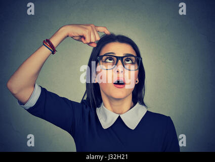 Closeup portrait young woman scratching head thinking about something looking up trying to recall isolated on grey wall background. Human facial expre Stock Photo