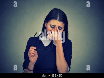 Woman with glasses rubbing her eyes feels tired isolated on gray wall  background. Young girl suffering from eye illness problem Stock Photo