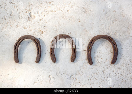 Three old rusty horseshoes hanging on a white wall, luck symbol Stock Photo