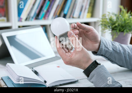 Man holds modern light bulb. Tablet PC in background. Stock Photo